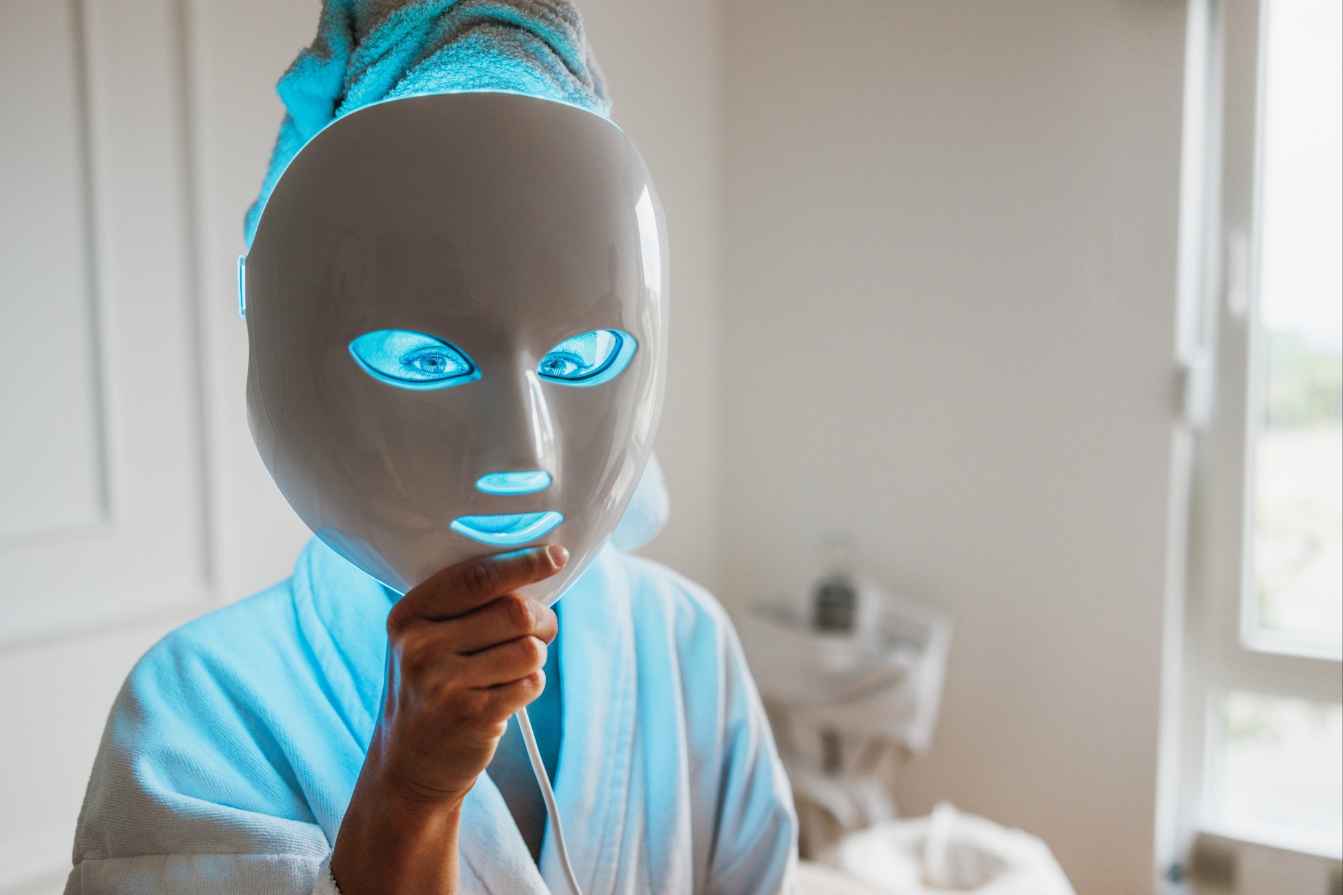 Person wearing a LED face mask in a bedroom setting